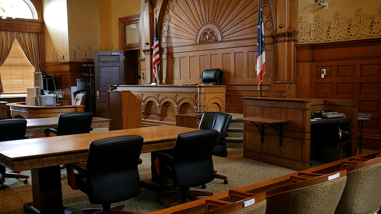Interior photo of an empty court room with wood paneling walls, and wood floor..